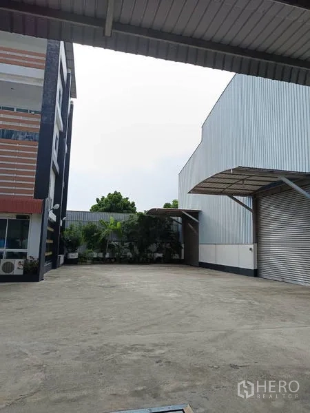 Factory for sale in Ban Phaeo, Samut Sakhon - Open yard between office block and warehouse with roller shutter door and canopy.