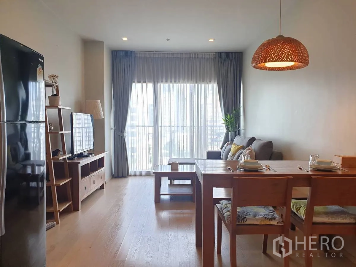 Condominium for rent or sale in Bangkok - Bright open-plan living and dining area with floor-to-ceiling windows, wood furniture and city views.