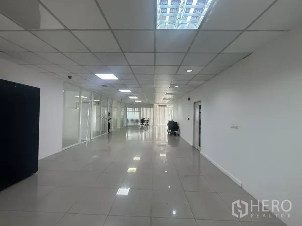 办公空间 出租在Huai Khwang, Bangkok - 宽敞的开放式办公走廊，玻璃隔间、亮面地砖与网格天花灯。