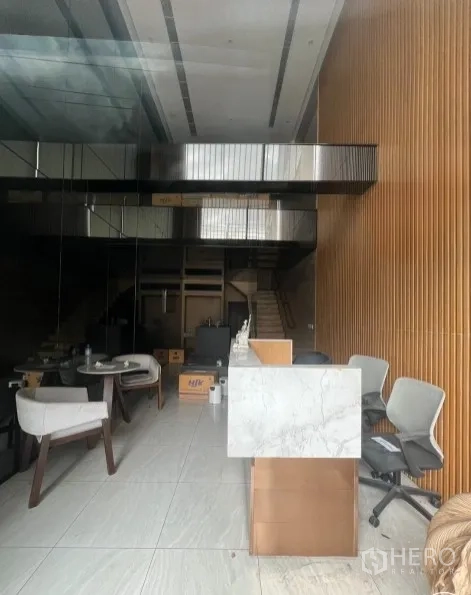 店屋 出租在Watthana, Bangkok - 一层室内挑高空间，石纹接待台、木条墙面，设有夹层与楼梯。