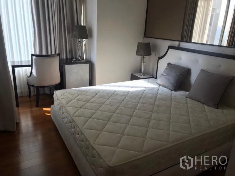 Condominium for rent in Pathum Wan, Bangkok - Spacious master bedroom featuring a large mattress, bedside tables with lamps, work desk by the window and wood flooring.