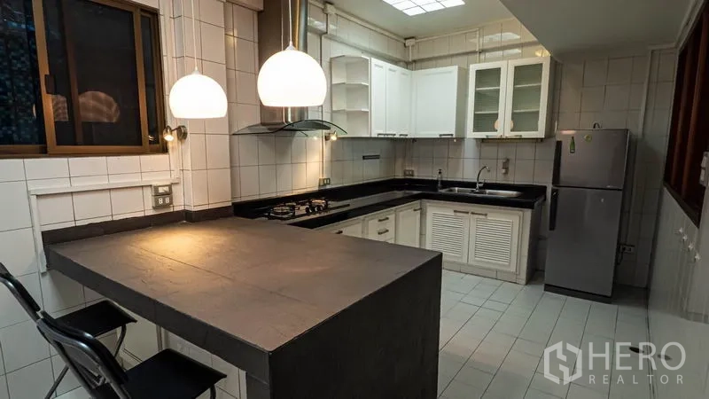 Townhouse for rent in Khlong Toei, Bangkok - Fitted kitchen with L‑shaped counters, gas hob, range hood and breakfast bar with pendant lights.