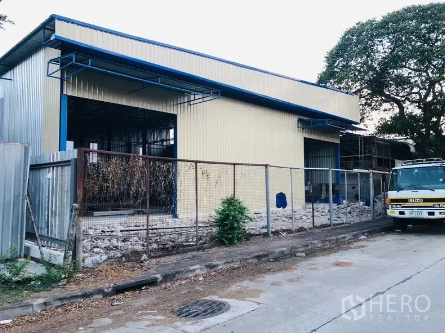 货栈 出租在Wang Thonglang, Bangkok - 黄色金属屋面蓝色边框的仓库外观，带围栏与宽敞装卸口的街景。