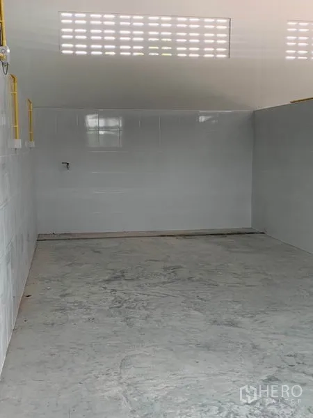 Warehouse for rent or sale in Thanyaburi, Pathum Thani - Empty bay with tiled wall panels, ventilation slots and smooth concrete slab.