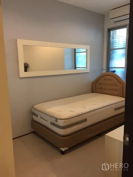 Condominium for rent in Khlong Toei, Bangkok - Compact second bedroom with single bed, long wall mirror and window.