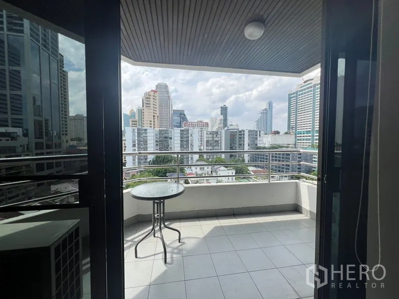 Condominium for rent or sale in Khlong Toei, Bangkok - Private balcony with railings and a small round table facing the Bangkok skyline.