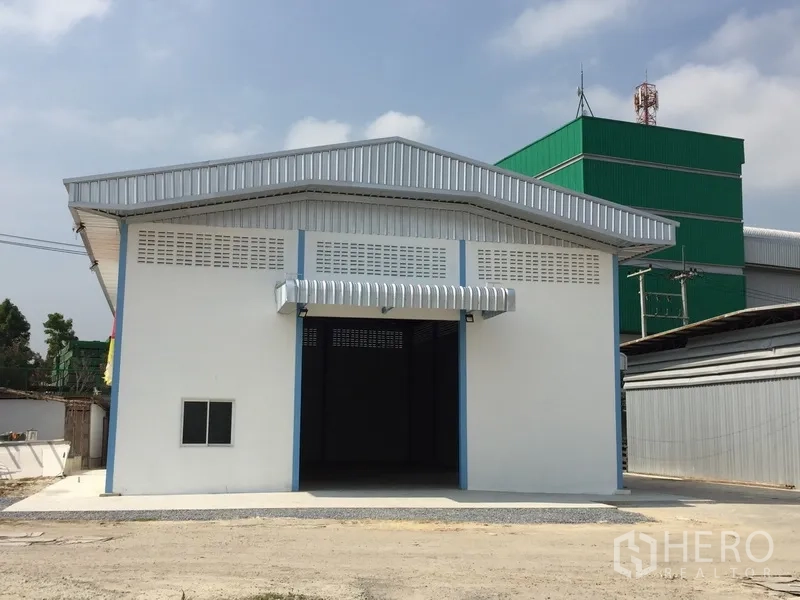 工厂 出租在Pathum Thani - 厂房正立面，金属屋顶与雨棚，宽阔入口和混凝土前坪。