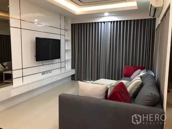 独立式住宅 出租在Bang Phli, Samut Prakan - 客厅明亮，内置电视墙、灰色窗帘、吊顶灯光与L形沙发。