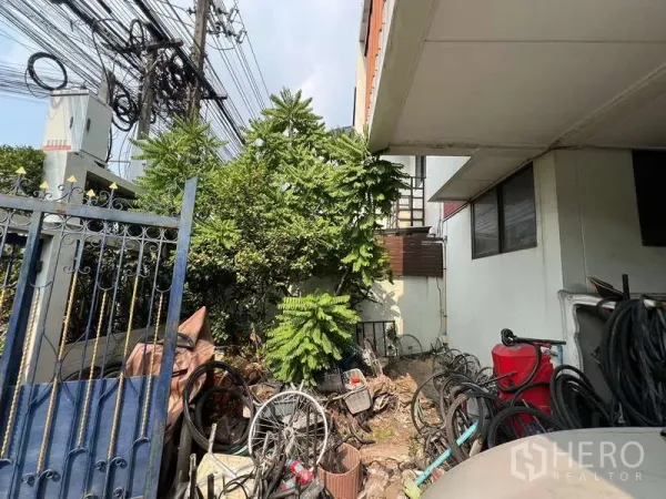 Detached House for sale in Suan Luang, Bangkok - Side yard beside the house with mature trees and a gated boundary wall.