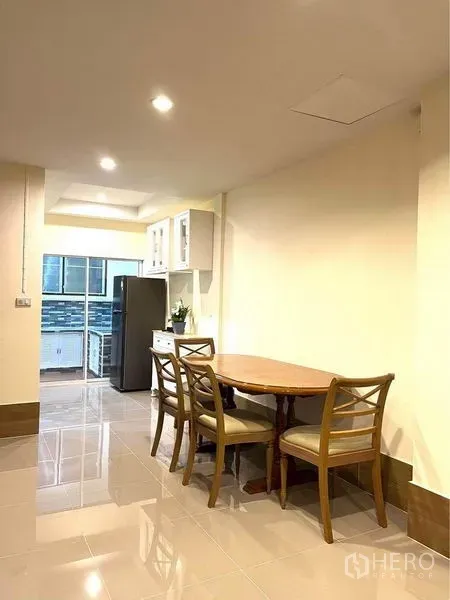 Townhouse for rent in Bang Na, Bangkok - Dining area with round wooden table and chairs beside the kitchen and refrigerator.
