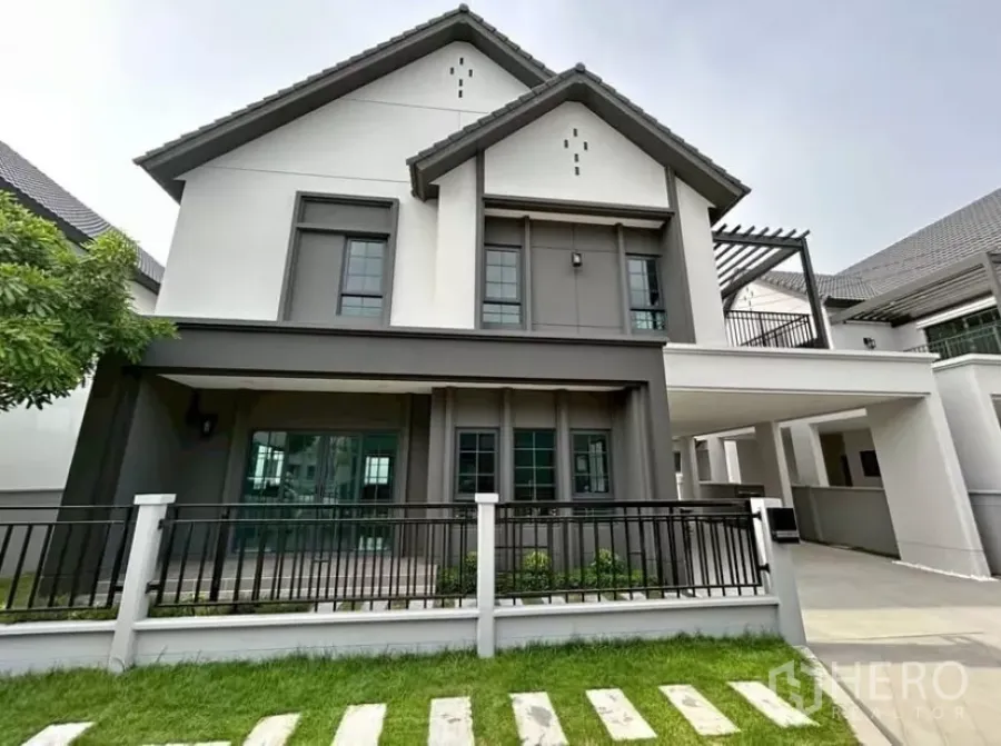 Detached House for rent in Bang Phli, Samut Prakan - Modern two-storey detached house with grey and white facade, gable roof, small lawn and front fence.