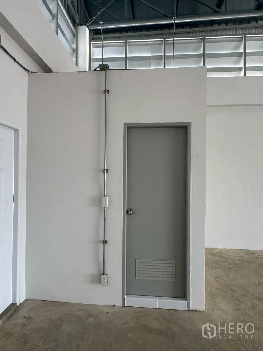 Warehouse for rent or sale in Nong Chok, Bangkok - Interior corner of warehouse showing white utility room with door and exposed electrical conduit.