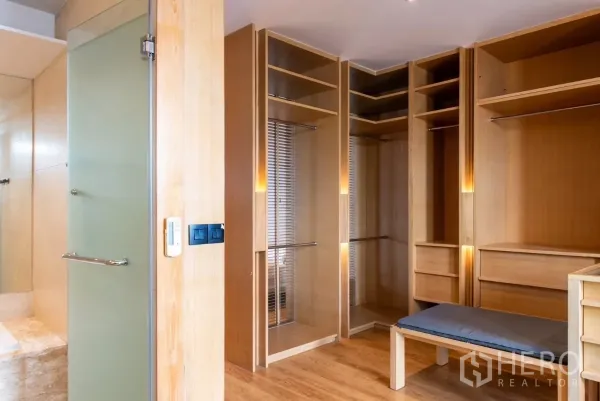 Townhouse for rent in Lat Phrao, Bangkok - Built-in wooden walk-in closet beside a frosted glass bathroom door.
