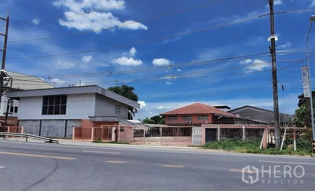 Warehouse for rent in Lam Luk Ka, Pathum Thani - Street-facing gated industrial compound with warehouse and office buildings in Lam Luk Ka under a blue sky.