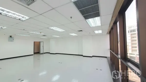 Office Space for rent in Watthana, Bangkok - Open office area with long row of windows, fluorescent lighting, ceiling air vents, and a doorway to an inner room.