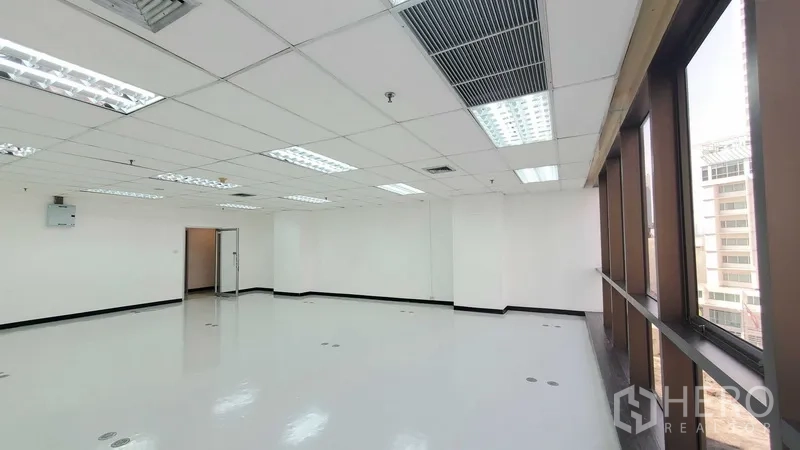 Office Space for rent in Watthana, Bangkok - Open office area with long row of windows, fluorescent lighting, ceiling air vents, and a doorway to an inner room.