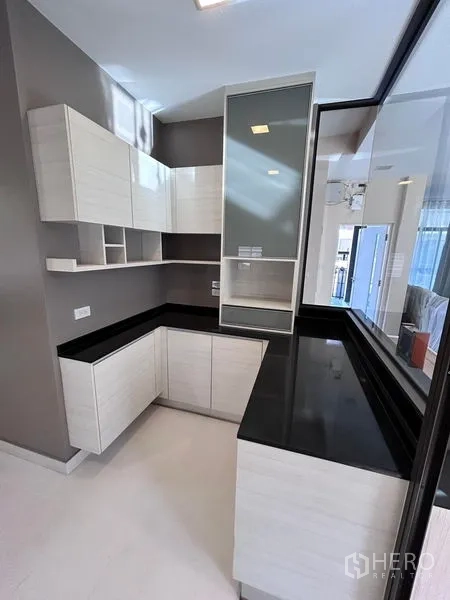 Detached House for rent or sale in Prawet, Bangkok - Kitchen corner cabinetry with black stone counters and glass display.