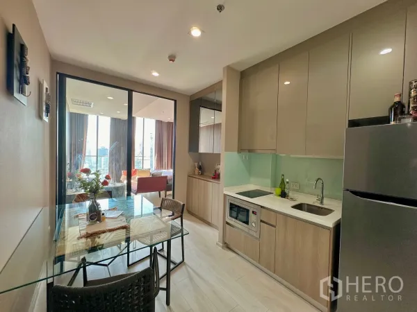 Condominium for rent in Pathum Wan, Bangkok - Modern kitchen with built-in cabinets, glass backsplash and dining table.