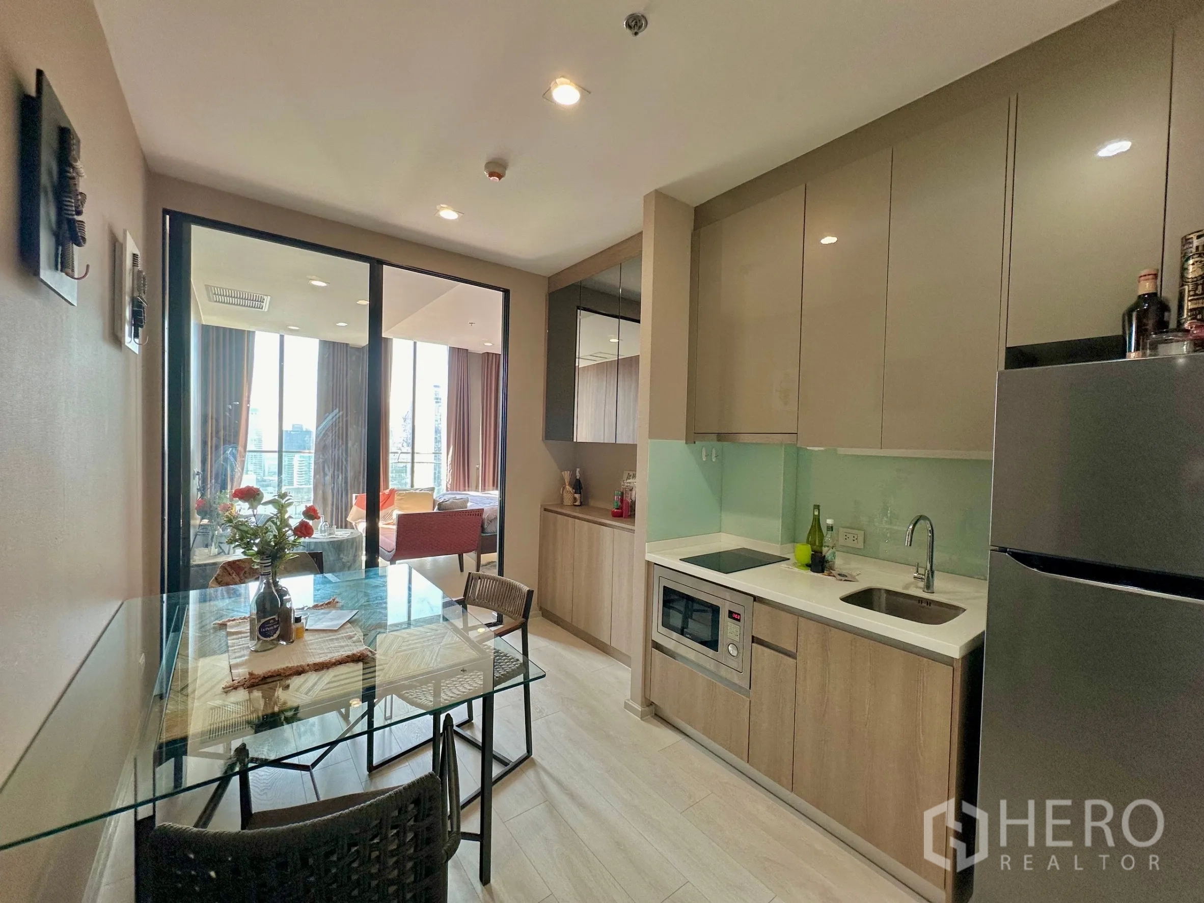 Condominium for rent in Pathum Wan, Bangkok - Modern kitchen with built-in cabinets, glass backsplash and dining table.