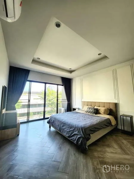 联排别墅 出租在Watthana, Bangkok - 主卧带托盘天花，木纹地板，落地推拉门通往阳台。