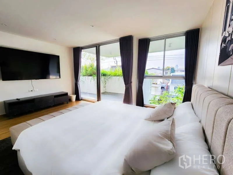 Home Office for rent in Phra Khanong, Bangkok - Bedroom with large TV and sliding doors opening to a leafy balcony.