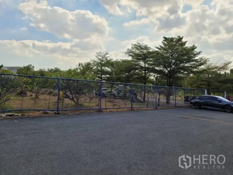 Warehouse for rent in Phra Khanong, Bangkok - Fenced outdoor parking area with asphalt surface and mature trees at a warehouse in Phra Khanong, Bangkok.