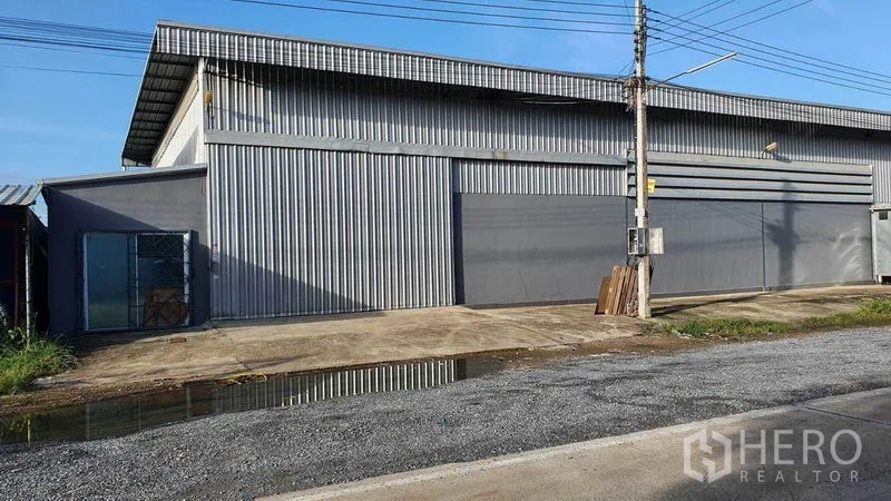 Warehouse for rent in Pathum Thani - Metal-clad warehouse exterior with wide sliding doors and a concrete driveway.