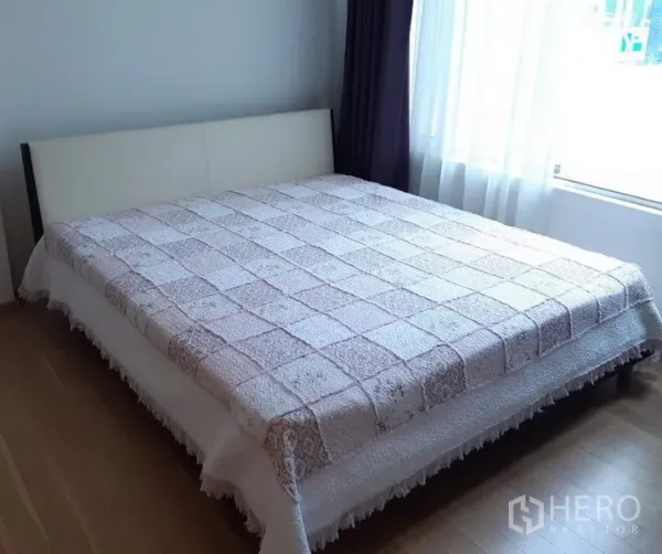 Condominium for rent in Khlong Toei, Bangkok - Cozy bedroom with a large bed, wood floors and abundant natural light from a wide window.