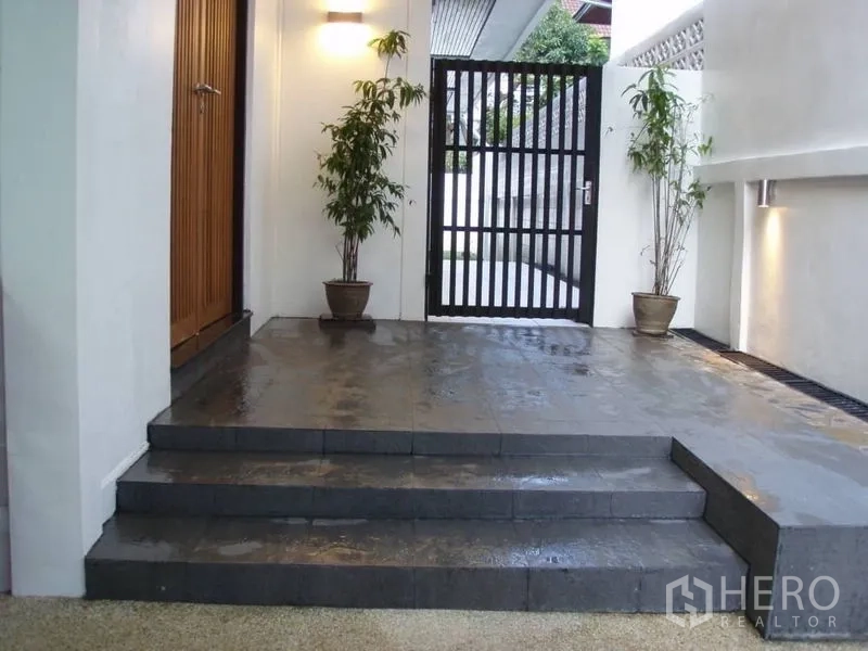 Detached House for rent in Huai Khwang, Bangkok - Covered entry with dark stone steps, potted plants, wall lights and secure metal gate