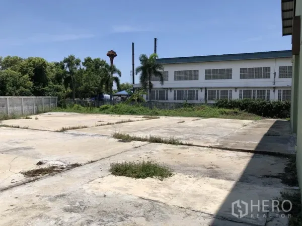 Factory for rent in Pathum Thani - Paved outdoor yard beside the factory with boundary wall and greenery.