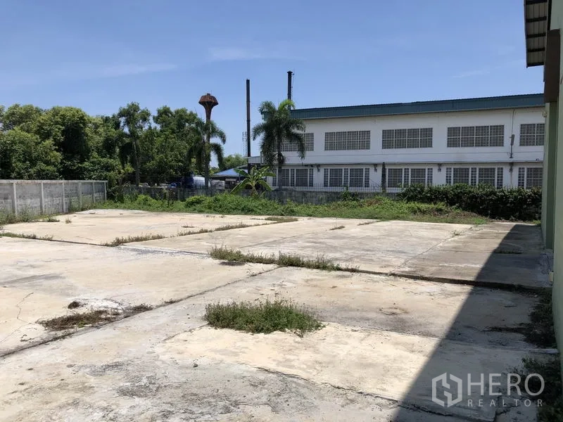 Factory for rent in Pathum Thani - Paved outdoor yard beside the factory with boundary wall and greenery.