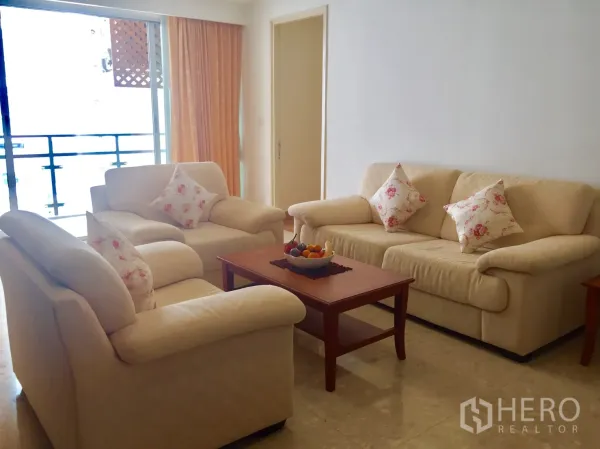 Condominium for rent in Khlong Toei, Bangkok - Living room with cream sofas, coffee table and sliding doors to a balcony.