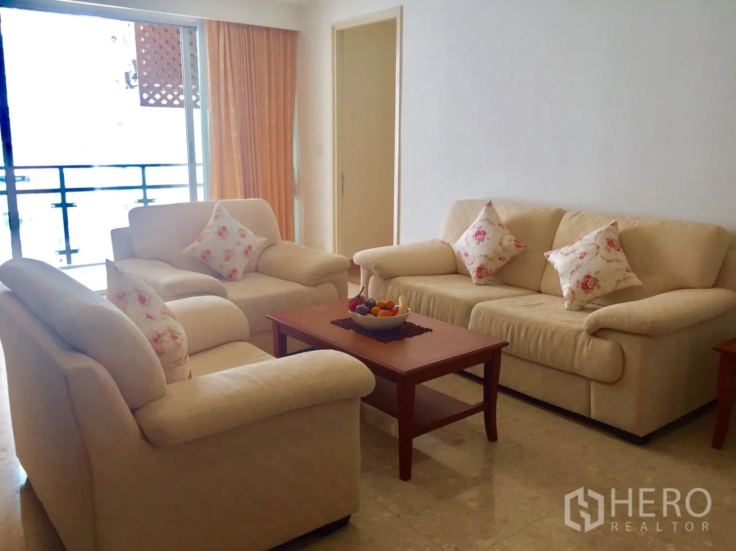 Condominium for rent in Khlong Toei, Bangkok - Living room with cream sofas, coffee table and sliding doors to a balcony.
