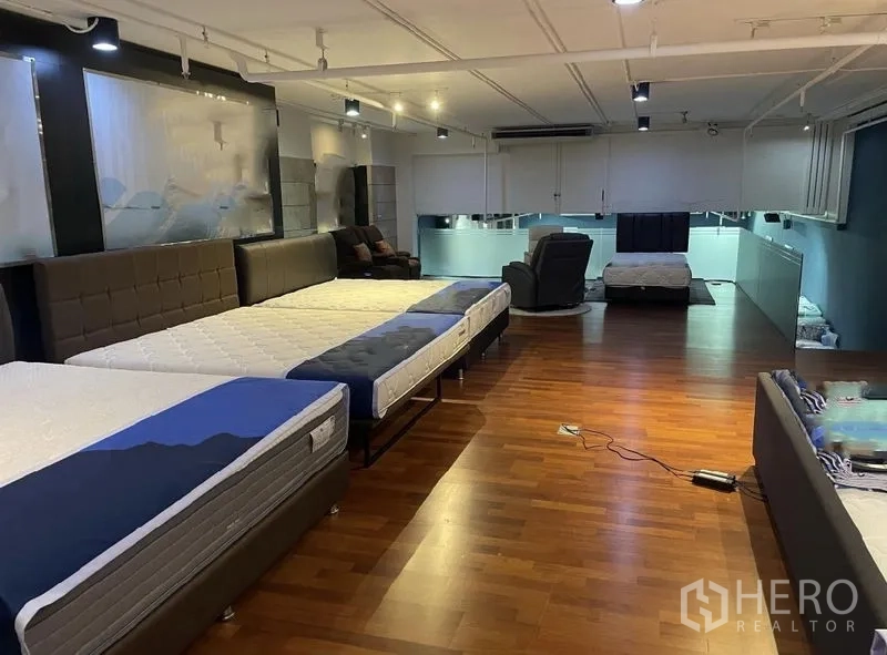 Retail Space for rent - Open-plan retail space with mattresses on display, warm wood flooring, ceiling track lights and a rear mezzanine with glass panels.
