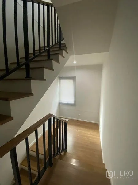 Townhouse for rent or sale in Saphan Sung, Bangkok - Stairwell with wooden steps and black metal handrails lit by a small window.