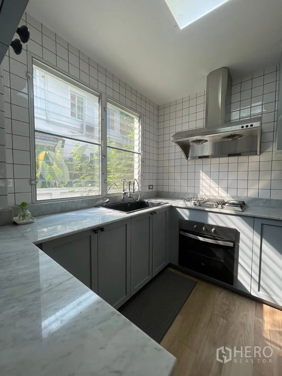 Detached House for rent in Prawet, Bangkok - L-shaped kitchen with marble counters, gas hob, oven and range hood under skylight.