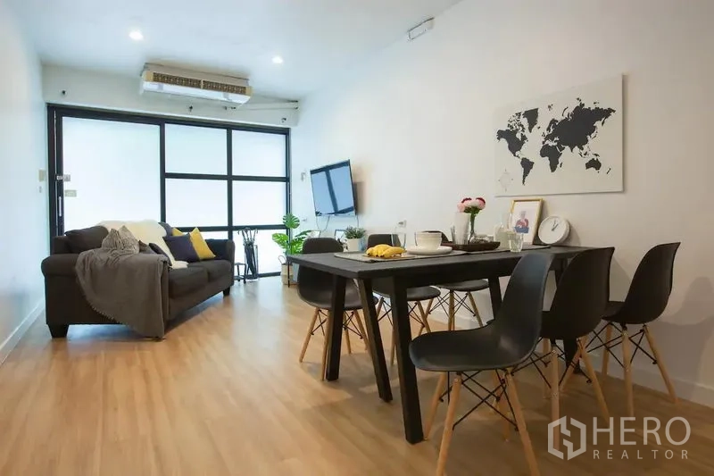 Townhouse for rent in Sathon, Bangkok - Bright living and dining area with sofa, TV, and large black-framed windows on wood flooring.