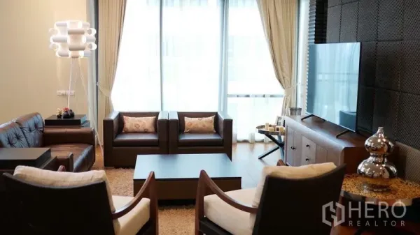 Condominium for rent in Khlong Toei, Bangkok - Cozy TV lounge with leather sofas, a large flat-screen and sheer curtains letting in daylight.