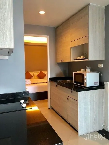 Condominium for rent in Khlong Toei, Bangkok - Compact condo kitchen with black countertops and light wood cabinets.