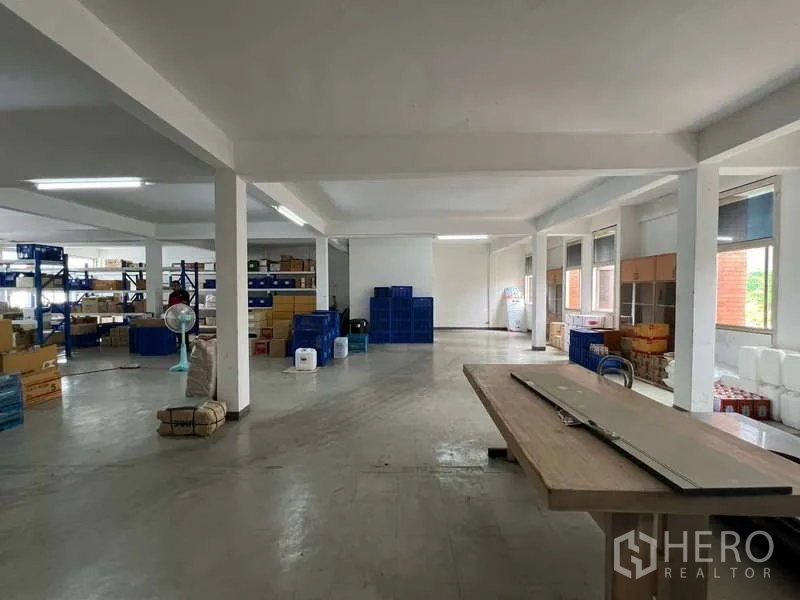 Shophouse for rent or sale in Khlong Toei, Bangkok - Spacious warehouse-style floor with large windows and shelving for stock.