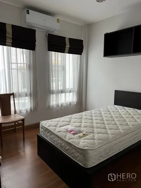 Townhouse for rent in Saphan Sung, Bangkok - Secondary bedroom with bed, wall shelf, tall windows with blinds and air conditioner.