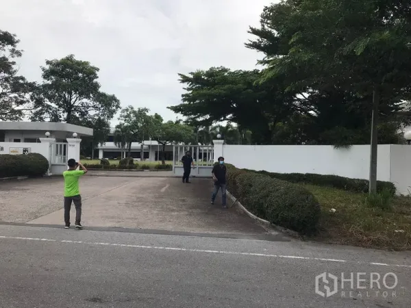 工厂 出租在Mueang Chon Buri, Chon Buri - 园区大门与门岗，车道宽敞，周边树木与绿篱景观