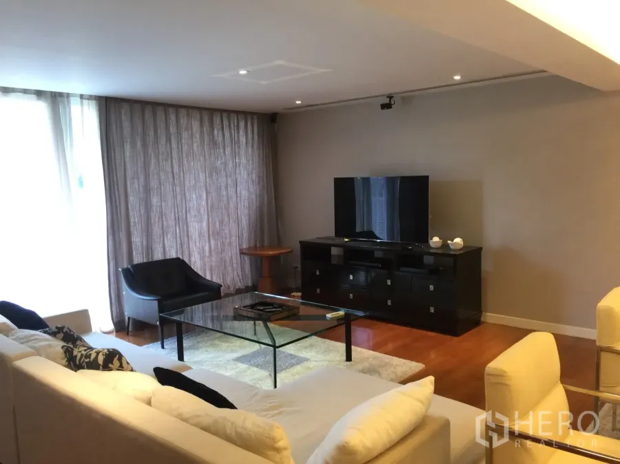 Condominium for rent in Watthana, Bangkok - Spacious living room with L-shaped sofa, glass coffee table, TV console and floor-to-ceiling curtains.