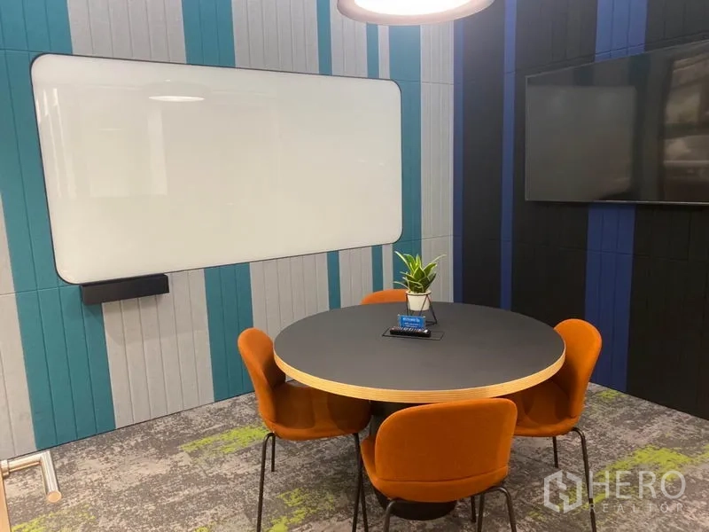 Office Space for rent in Pathum Wan, Bangkok - Huddle room with round table, orange chairs, whiteboard and wall-mounted screen.