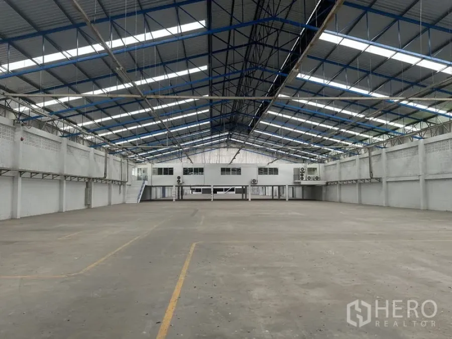 Factory for rent in Nonthaburi - Wide-span warehouse interior showing floor markings and mezzanine offices.
