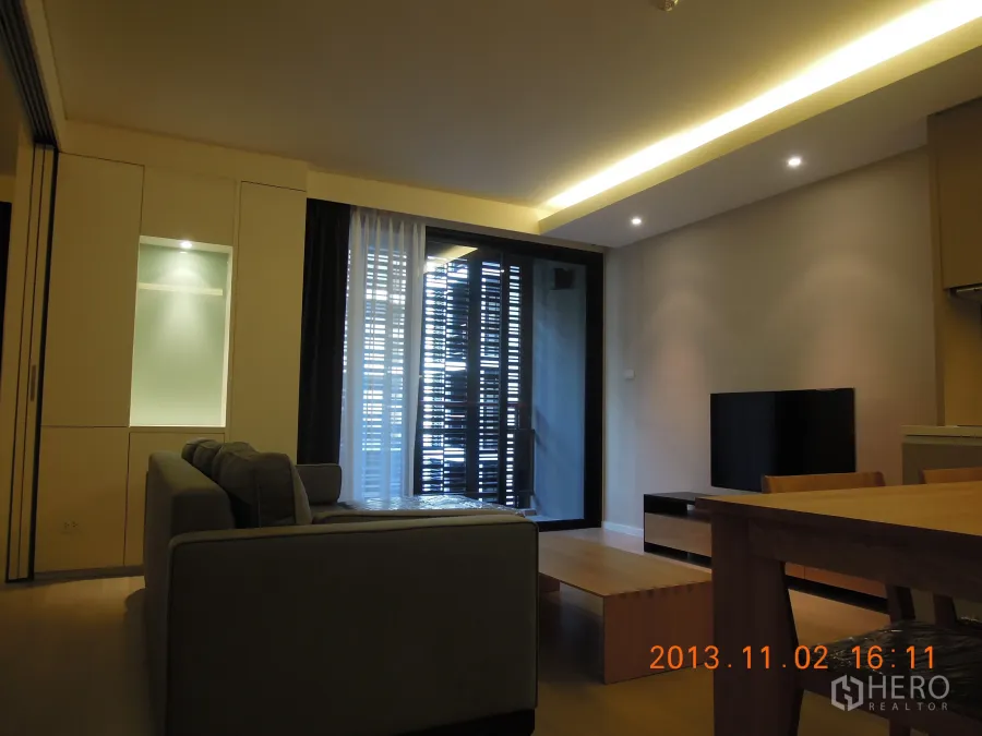 Condominium for rent in Watthana, Bangkok - Modern living room with sofa, TV, dining table, and a balcony with louvered screen in a Sukhumvit condo.
