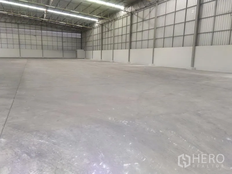 Warehouse for rent in Bang Phli, Samut Prakan - Spacious empty warehouse interior with high clear-span steel roof, bright strip lighting and concrete floor.