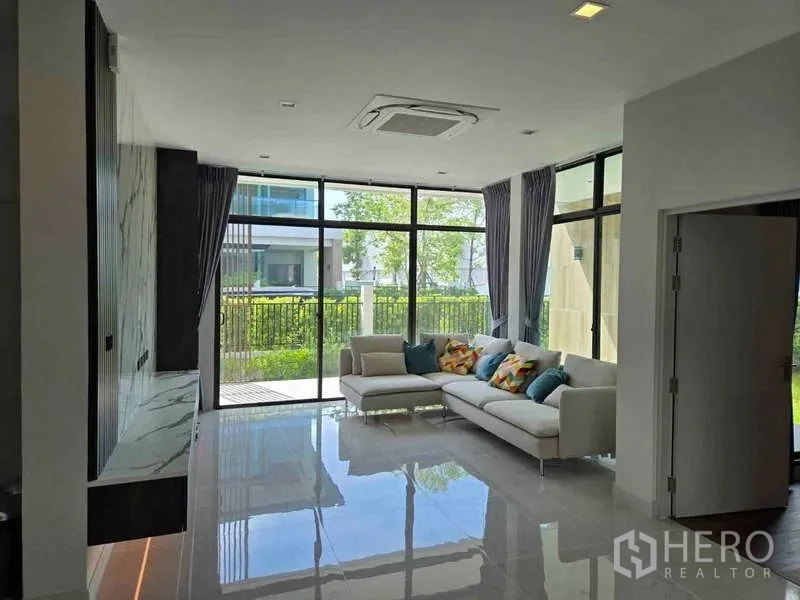 独立式住宅 出租在Bang Phli, Samut Prakan - 客厅落地窗与L形沙发，亮面地砖通向花园。