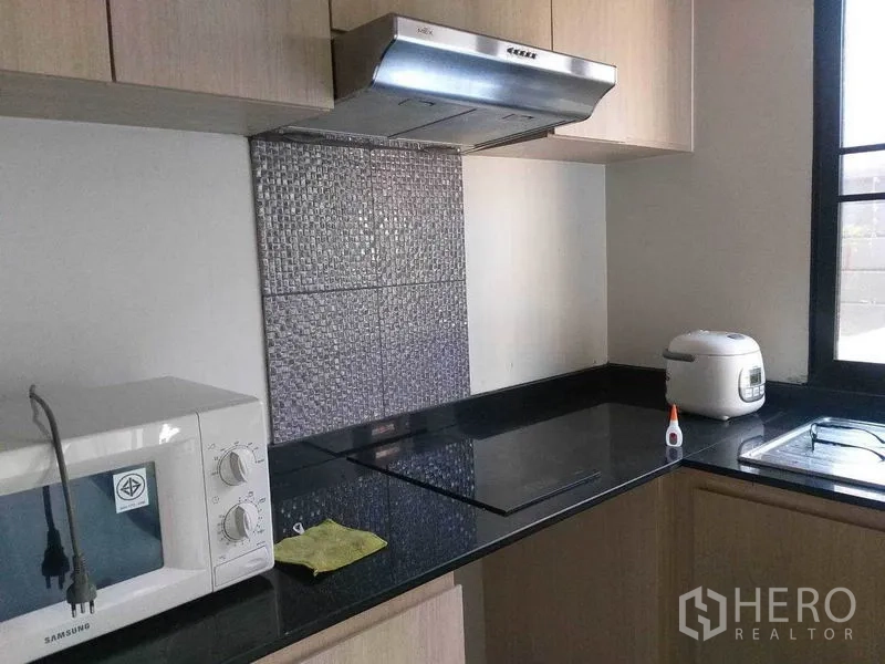 Townhouse for rent in Suan Luang, Bangkok - Modern kitchen with black granite countertop, induction hob, stainless hood, microwave and sink by the window.