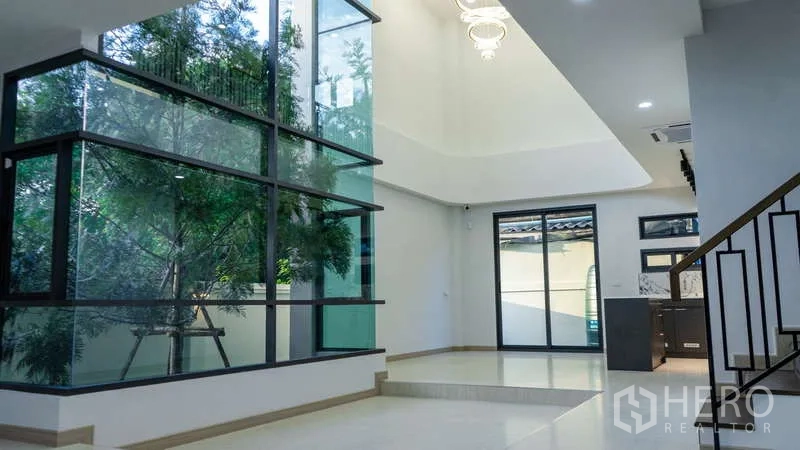 Detached House for rent or sale in Suan Luang, Bangkok - Open living area with a large glazed wall, chandelier and metal balcony railing